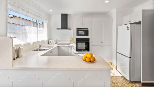 A modern kitchen with white cabinetry, a central island, a built-in oven, and a refrigerator.