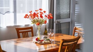 A wooden dining table with a vase of red flowers, a bottle of wine, and glasses.