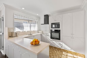 Une cuisine moderne avec des meubles blancs, un four encastré, un four à micro-ondes et un panier à fruits posé sur le plan de travail.