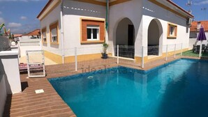 Un espace piscine avec une terrasse carrelée, un bâtiment blanc agrémenté de bordures jaunes et un patio clôturé.