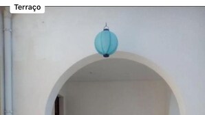 Un espace extérieur aménagé avec un canapé et des fauteuils placés sous une arche, une lanterne suspendue et une plante en pot.