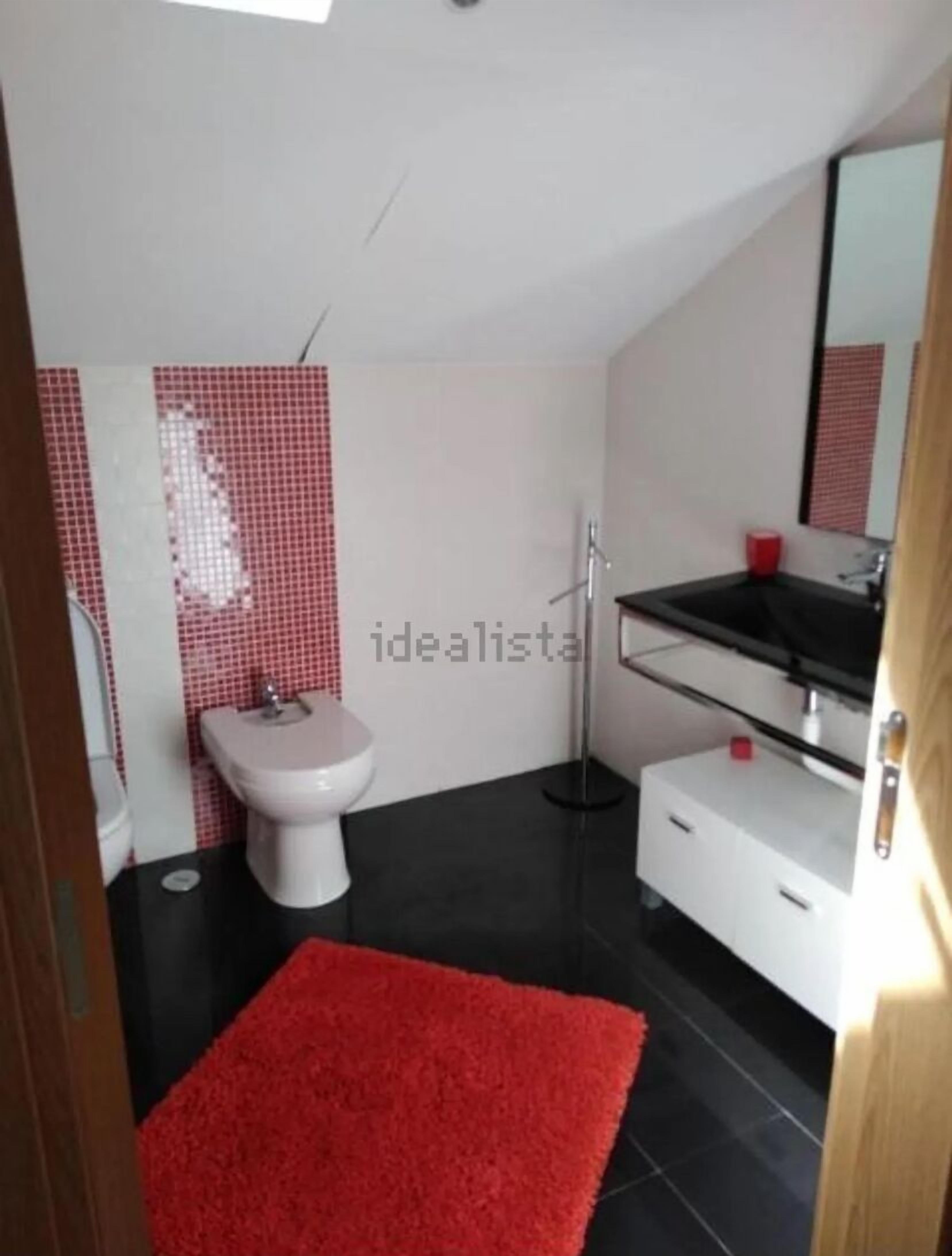 Ein modernes Badezimmer mit schwarzem Boden, weißen Wänden, einem roten Teppich, einer weißen Toilette und einem schwarzen Waschbecken.
