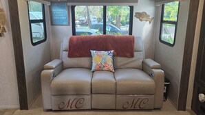 A cozy RV interior with a beige sofa, a red blanket, and a decorative pillow. - Sunshine Serenity @ Crystal River, Florida (Crystal River)