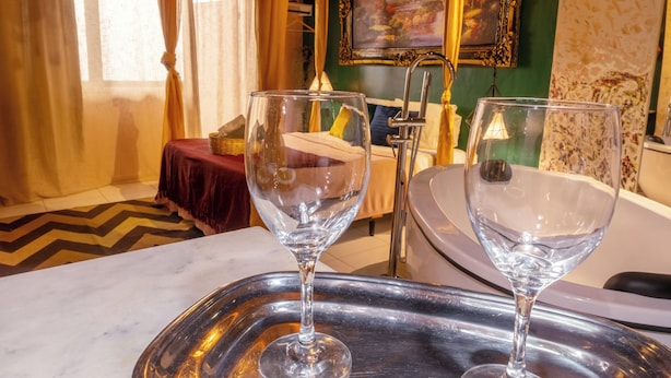 A hotel room with a marble floor, a bed with a red bedspread, two empty wine glasses on a tray, a painting on the wall, and a bathroom with a bathtub. - Charming Loft in the Historic Center (Centro Histórico Salvador)