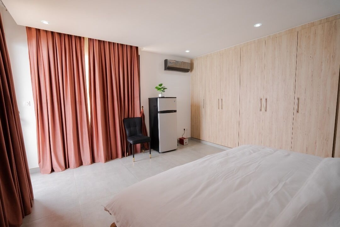 A hotel room with a bed, a desk with a chair, a wardrobe, and an air conditioning unit.