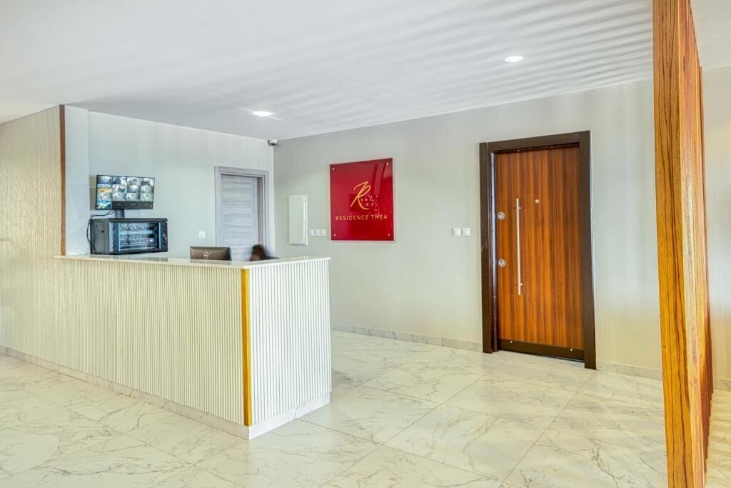 Una zona de recepción con un mostrador blanco, un televisor montado en la pared y una puerta de madera.