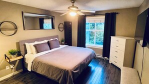 Een slaapkamer met een bed, een plafondventilator, een dressoir, een spiegel en een raam met gordijnen.