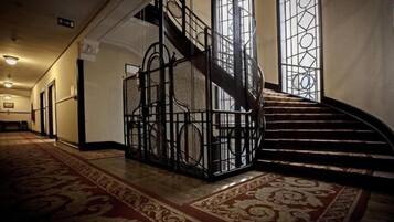 Uma escadaria imponente com grades de metal elaboradas e piso revestido, que leva a um patamar.