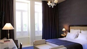 Et hotelværelse med en seng, en sofa, et skrivebord og en lysekrone.