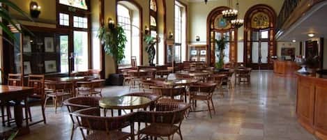 A spacious dining area with high ceilings, arched windows, and a variety of seating arrangements including tables and chairs.