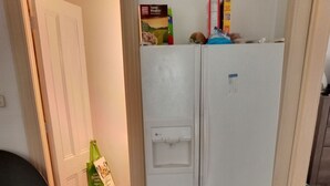 Eine kleine Küche mit einem weißen Kühlschrank, einer Tür zu einem anderen Raum und einem Fliesenboden.