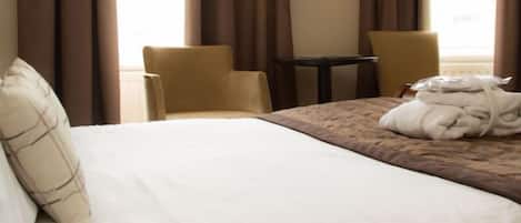 Quarto de hotel com cama, duas cadeiras, uma mesa pequena e janela com cortinas.