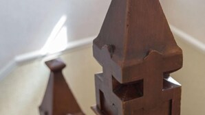 A close-up of a wooden architectural model with a pointed roof and a square base.