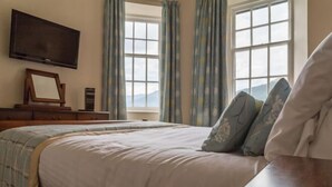A bedroom with a bed, a television mounted on the wall, a dresser, and a window with curtains.