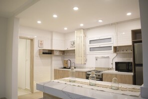A modern kitchen with white cabinetry, a marble countertop, a built-in microwave, and a stainless steel refrigerator.