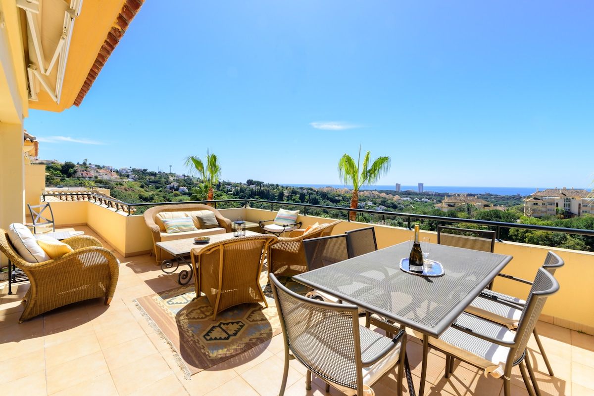 A terrace with outdoor furniture, a table with a bottle, and a view of the landscape.