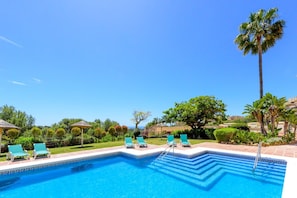 Una piscina con sillas de descanso y palmeras.