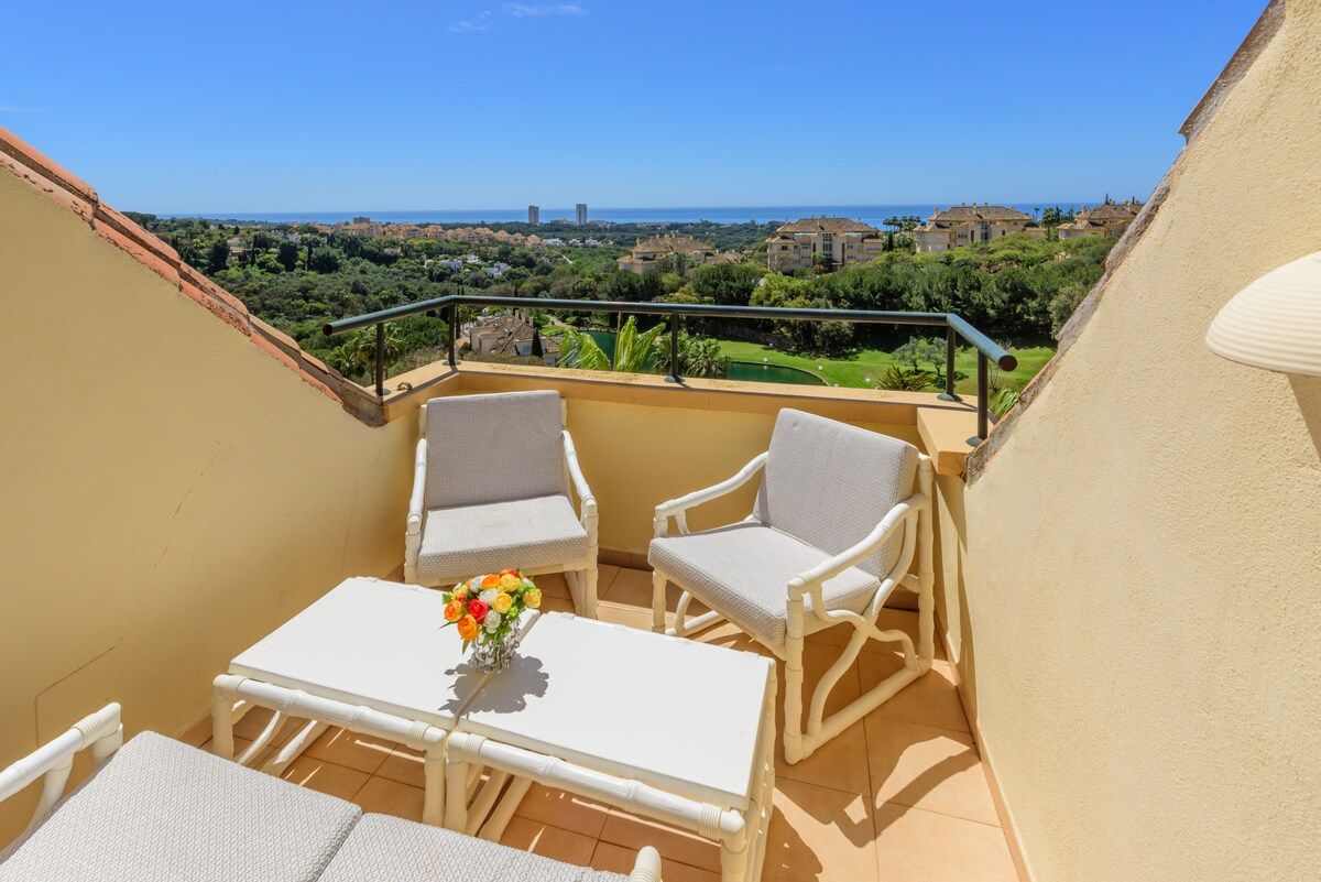 Un balcón con una mesa y dos sillas, con vistas a un paisaje costero.