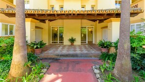 A hotel entrance with a checkered floor, potted plants, and a red pathway leading to the doors.