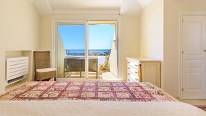 A bedroom with a large bed, a chair, a dresser, and a sliding glass door leading to a balcony.