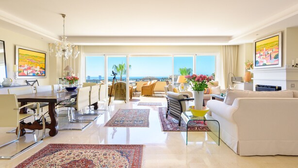 A spacious living area with a dining set, a sofa, and a balcony with a view.