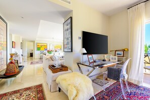 Una sala de estar moderna con un televisor de pantalla plana, un sofá blanco, una mesa de centro con objetos decorativos y una alfombra grande.