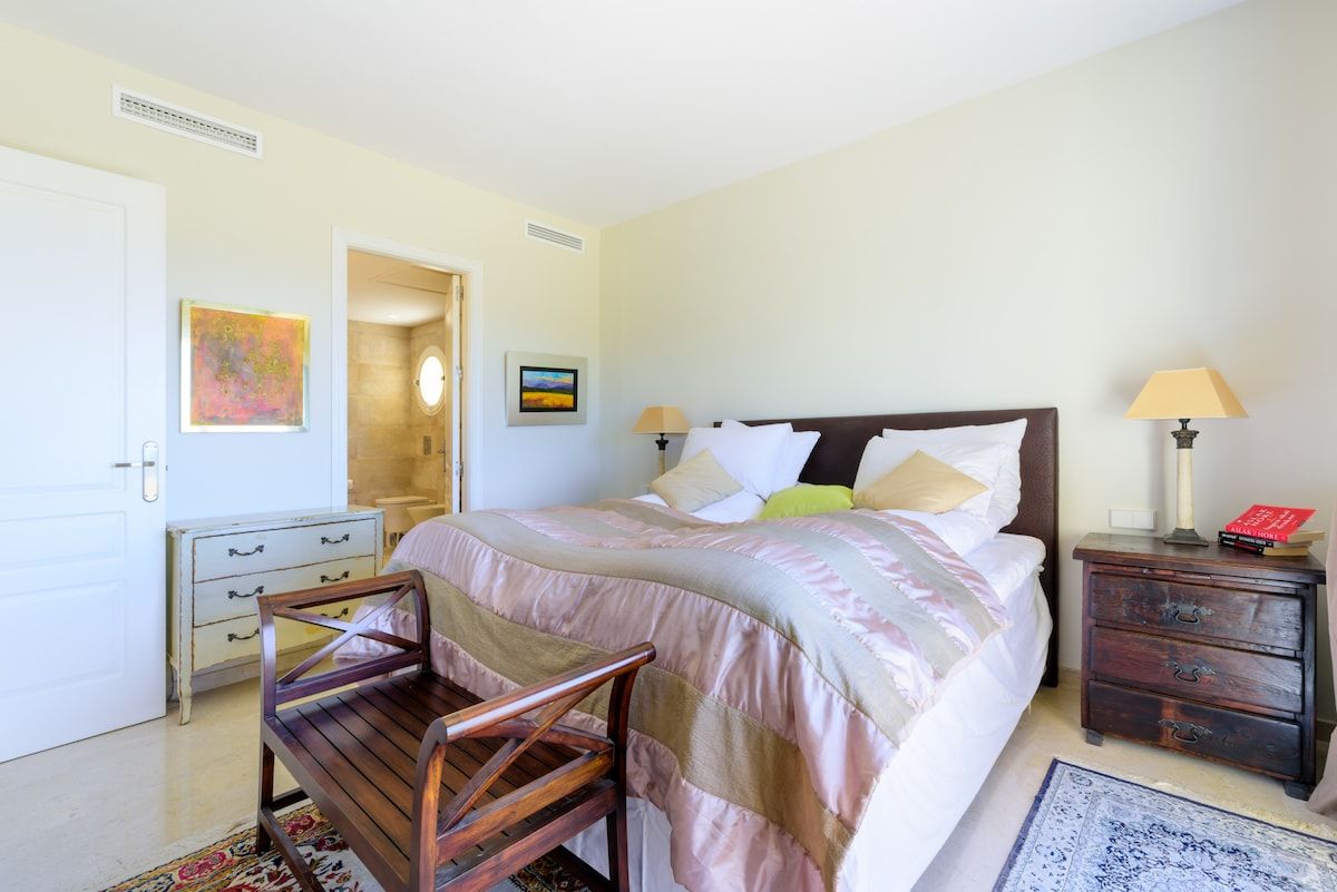 A bedroom with a bed, bedside tables, a chair, a rug, and artwork on the walls.