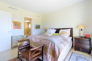 Een slaapkamer met een bed, nachtkastjes, een stoel, een vloerkleed en kunstwerken aan de muur.