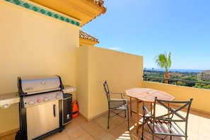 Een balkon met een barbecue, stoelen en een tafel.