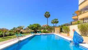 A swimming pool with lounge chairs, palm trees, and a building with balconies.