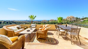 A terrace with wicker furniture, a table, and chairs, overlooking a scenic landscape.