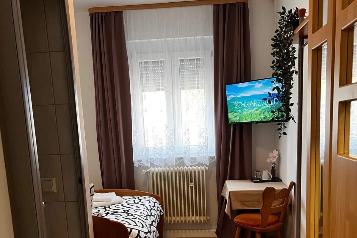Una habitación pequeña con cama, escritorio, silla, radiador y televisor.