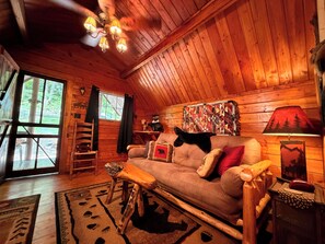 A cozy cabin interior with a wooden ceiling, a sofa with pillows, a lamp, and a window with curtains. - The Big Bear Cabin! Perfect getaway in the Smokey Mountains! (Cosby)