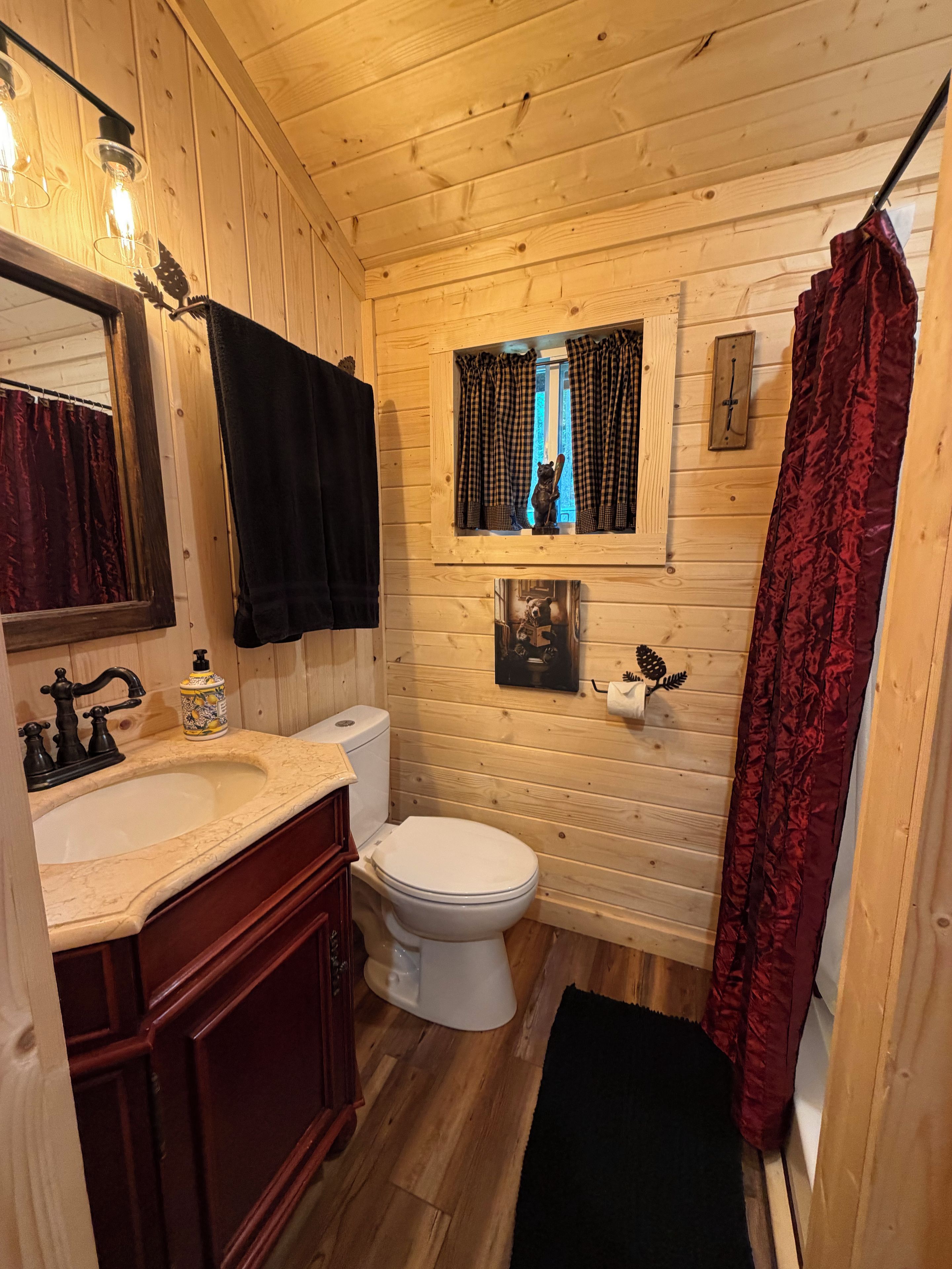 A wooden cabin bathroom with a sink, toilet, and a window with curtains.