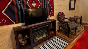 A cozy room with a television, wooden walls, a patterned tapestry, a chair, and a fireplace.