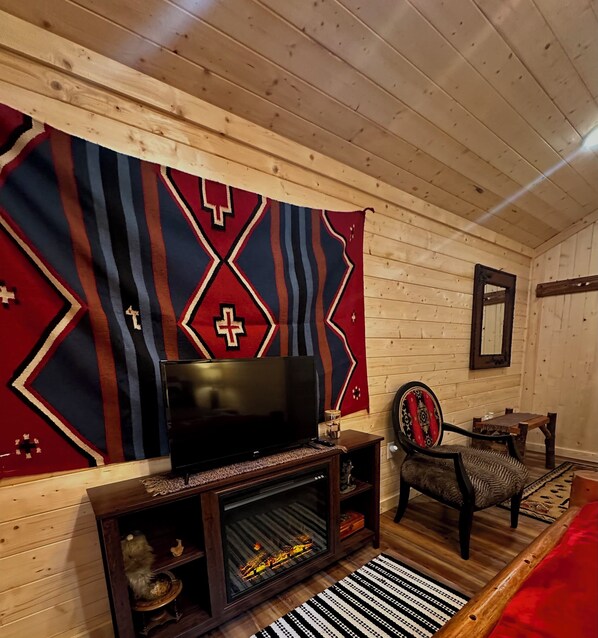 A cozy room with a television, wooden walls, a patterned tapestry, a chair, and a fireplace.