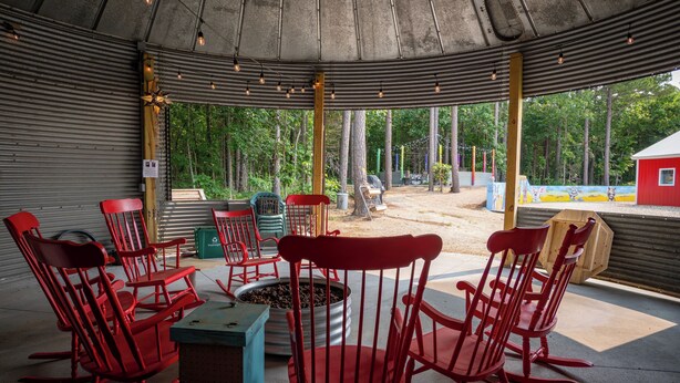 A covered outdoor seating area with red rocking chairs and a fire pit. - Hermann Grain Bins BNB  (Hermann)