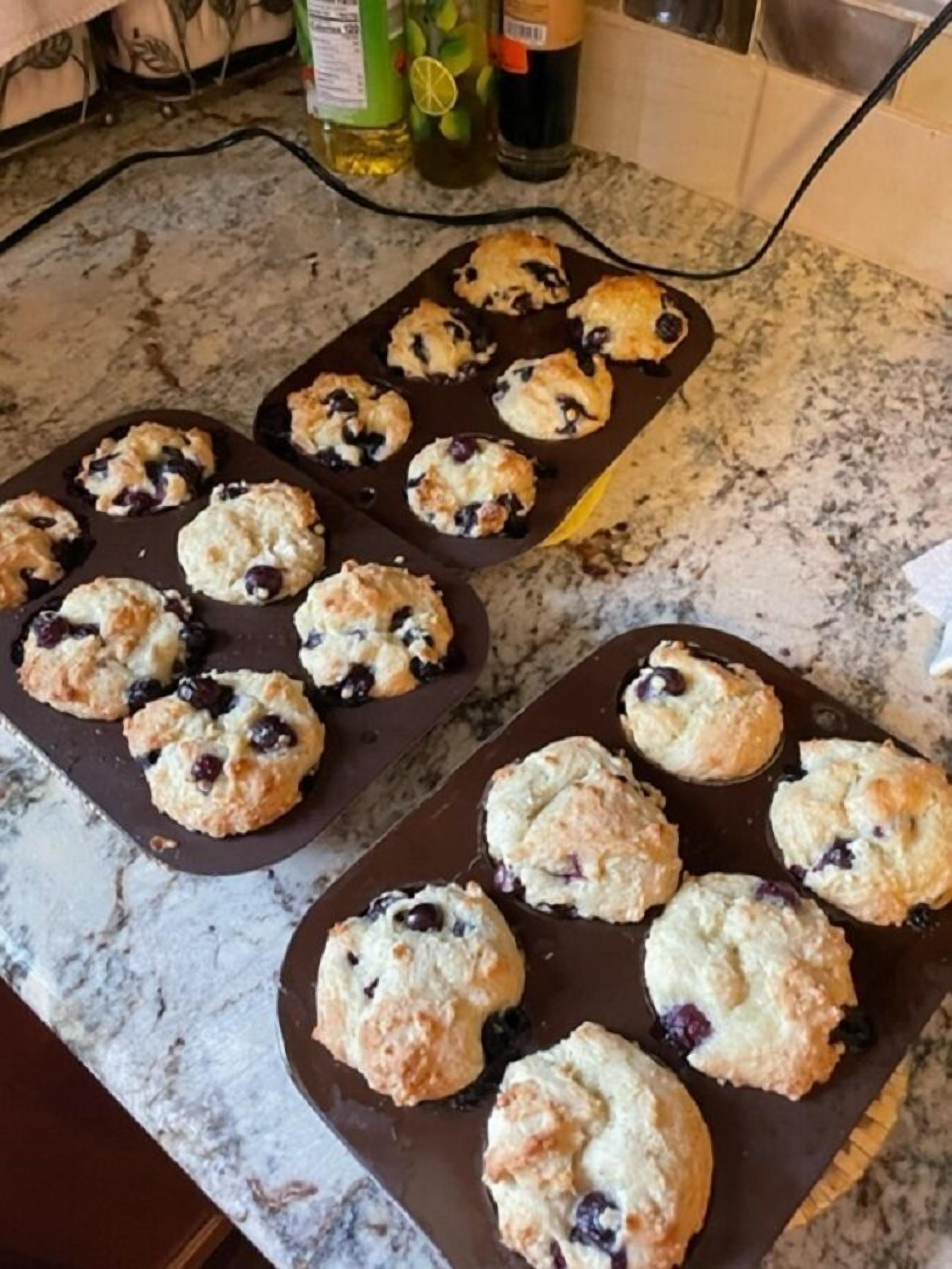 Uma bancada de cozinha com duas formas de muffins repletas de muffins de blueberry.