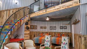 A spacious loft-style room with a curved staircase, wooden walls, and a loft bed area. - Hermann Grain Bins BNB  (Hermann)