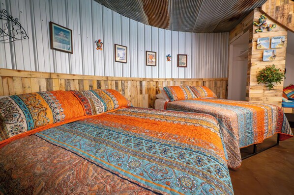 A room with two beds, each with patterned bedding. The walls are lined with framed pictures and a wooden headboard.