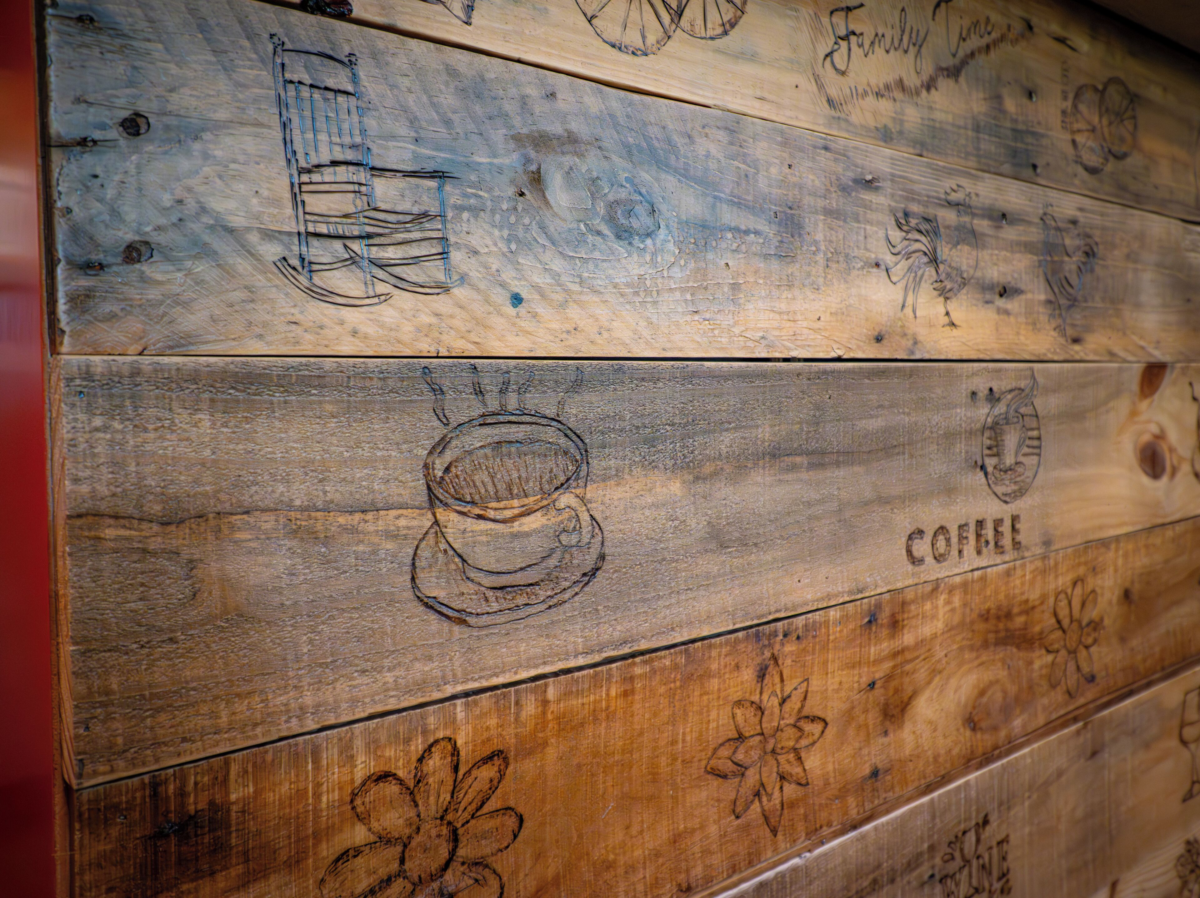 A wooden wall with various etched designs including a cup, a chair, and the word "COFFEE".