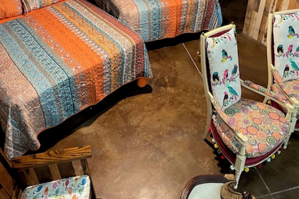 A rustic room with two wooden beds, a wooden chair with colorful patterns, and a metal-framed window.