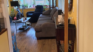 A living room with a sofa, a coffee table, and a TV. There is a window with plants and a view of the outside. - A little bit of Heaven! (Grand Forks)