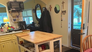 A kitchen with a wooden table, white cabinets, and a microwave. There is a door leading to a porch with a bench. - A little bit of Heaven! (Grand Forks)