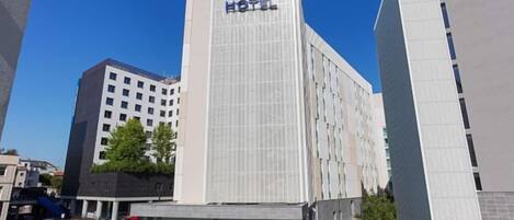 A modern hotel building with a prominent sign, large windows, and a parking lot.