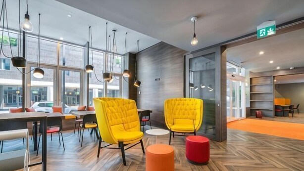 A modern interior with wooden flooring, yellow chairs, a red ottoman, and large windows. - Campanile Venice Mestre (Venice)