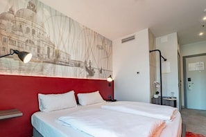 Une chambre d’hôtel avec un grand lit, un mur d’accent de couleur rouge et un tableau représentant un bâtiment historique.