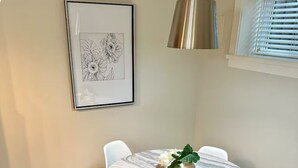 Un coin repas avec une table ronde, des chaises blanches, une plante en pot et une œuvre d’art florale encadrée accrochée au mur.