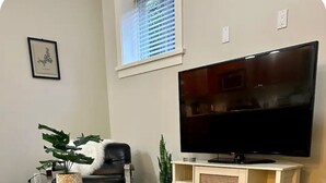 Un salon avec une table basse en verre, un canapé blanc, un téléviseur posé sur un meuble en bois et un tapis à motifs.
