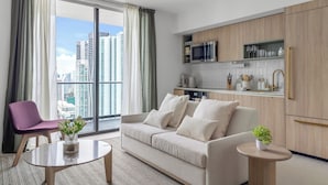 A modern living room with a sofa, a coffee table, and a purple chair. There is a kitchen area with wooden cabinets and a microwave. - 3701 - Kaseya Center 2 Bedroom Modern Apt with Pool & Gym in Downtown Miami (Miami)